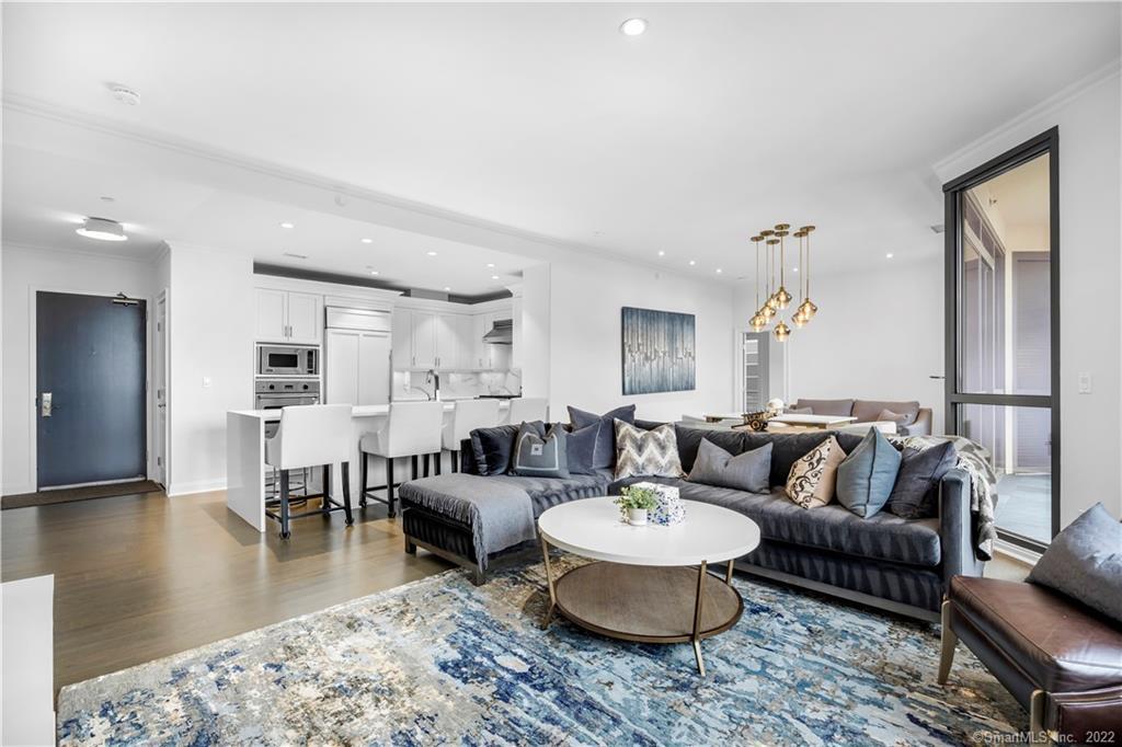 Open-plan condo living room with gray sectional, blue patterned rug, and white kitchen island.