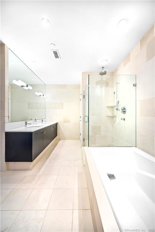 Bathroom with a dark vanity, mirrored wall, and glass-enclosed shower beside a white bathtub.