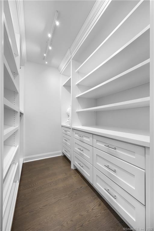 Walk-in closet with white built-in shelves and drawers and dark wood flooring.