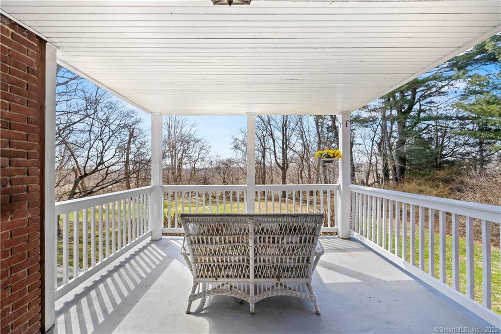 Covered porch with a wicker loveseat overlooking a lawn and leafless trees.