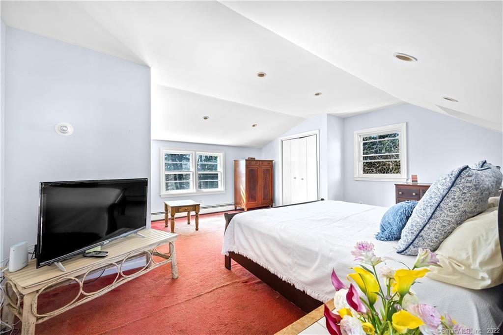 Bedroom with a white bed, blue patterned pillows, red rug, television, and wooden armoire.