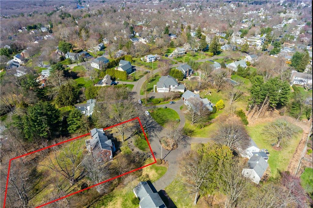 Aerial view of a wooded residential lot outlined in red among neighborhood homes.
