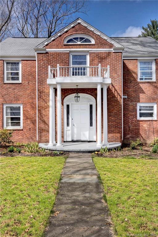Red brick house with a white portico, balcony, arched window, and stone walkway.