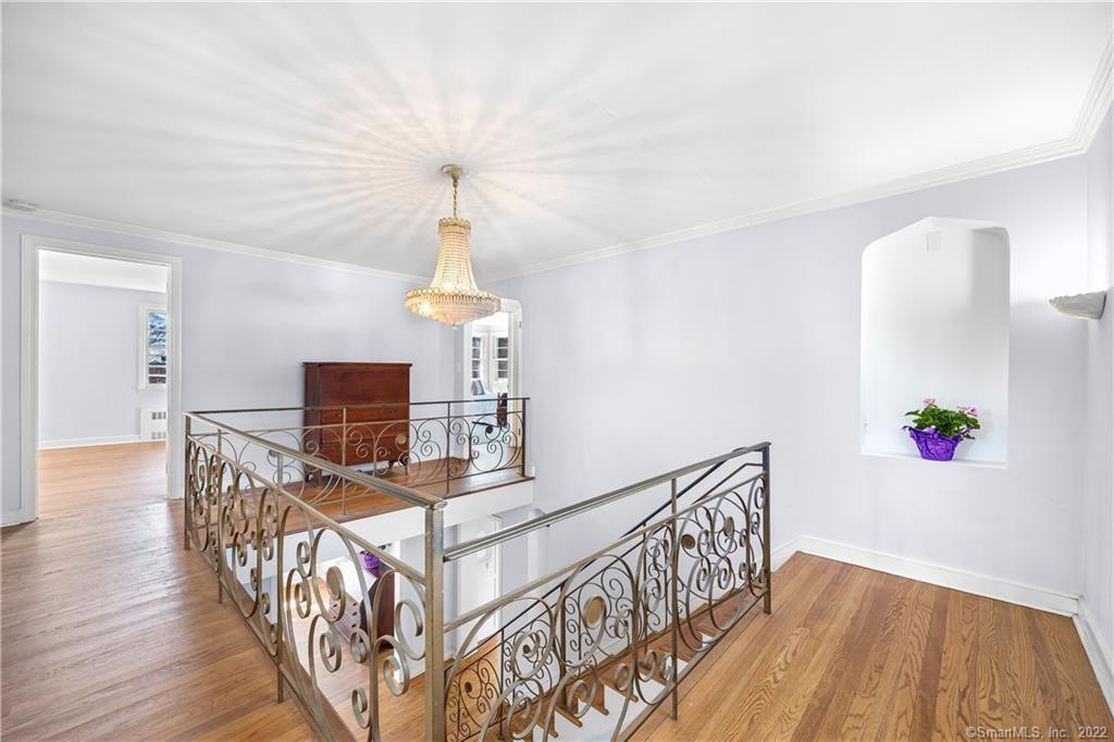 Upstairs landing with ornate iron railings, hardwood floors, and a crystal chandelier.