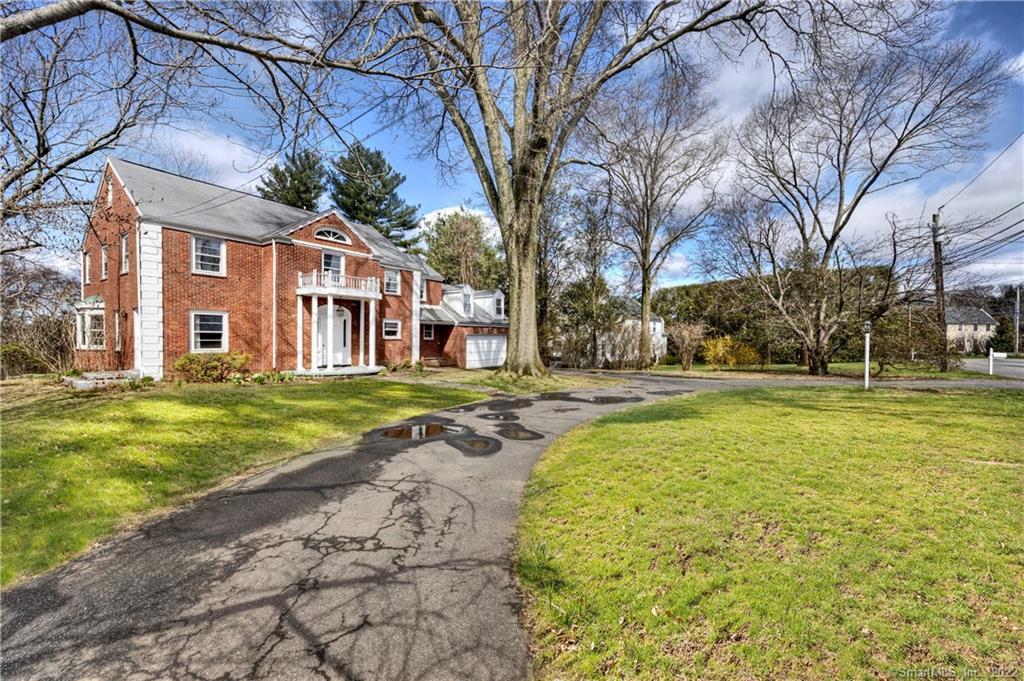 Red-brick Colonial home with a white entrance balcony, attached garage, and curved driveway.