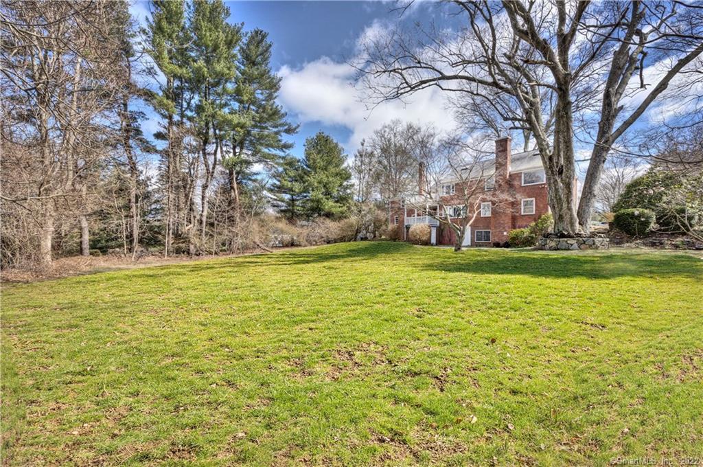 Red brick house beyond a broad green lawn, framed by mature trees.