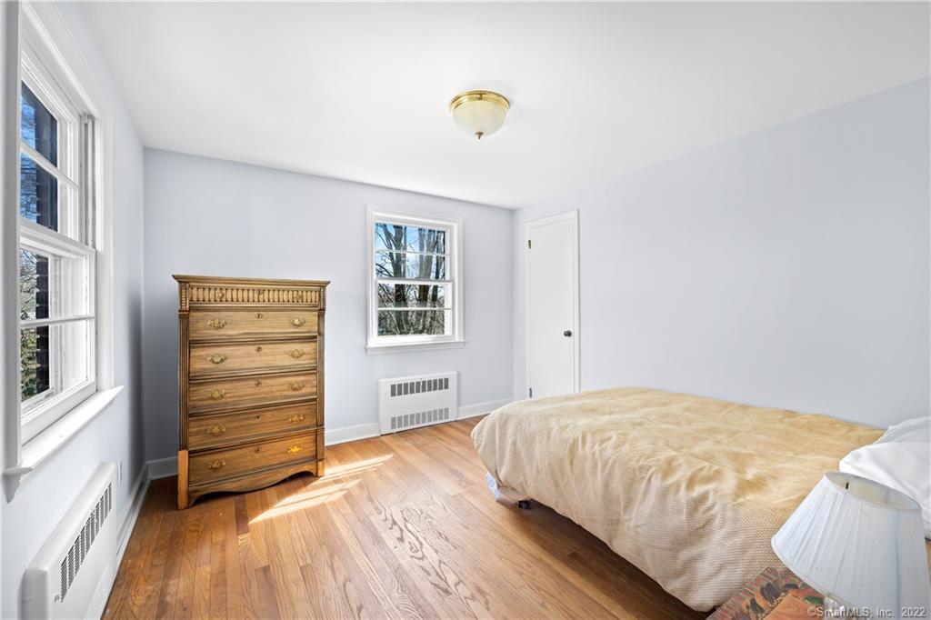 Bedroom with hardwood floors, tall windows, a wooden dresser, and a bed with a beige coverlet.