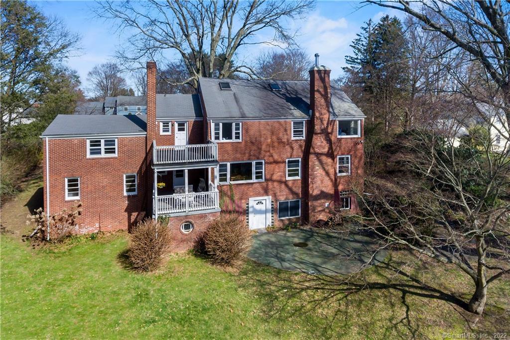 Red-brick home with two balconies overlooking a lawn and paved area, seen from above.