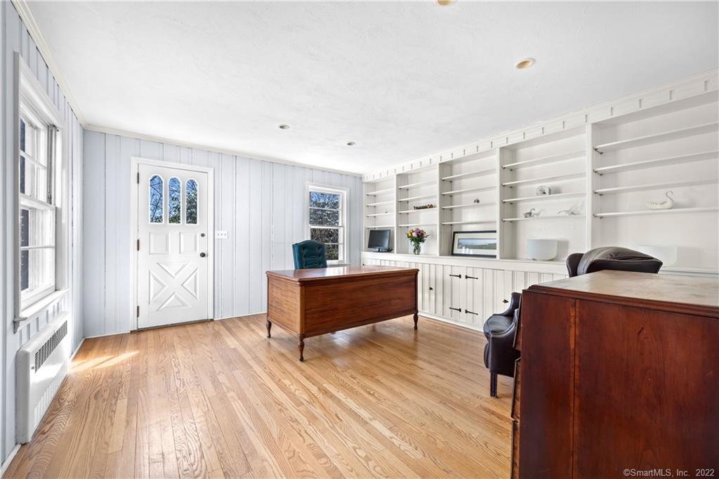 Home office with built-in white shelving, two wooden desks, and hardwood floors.