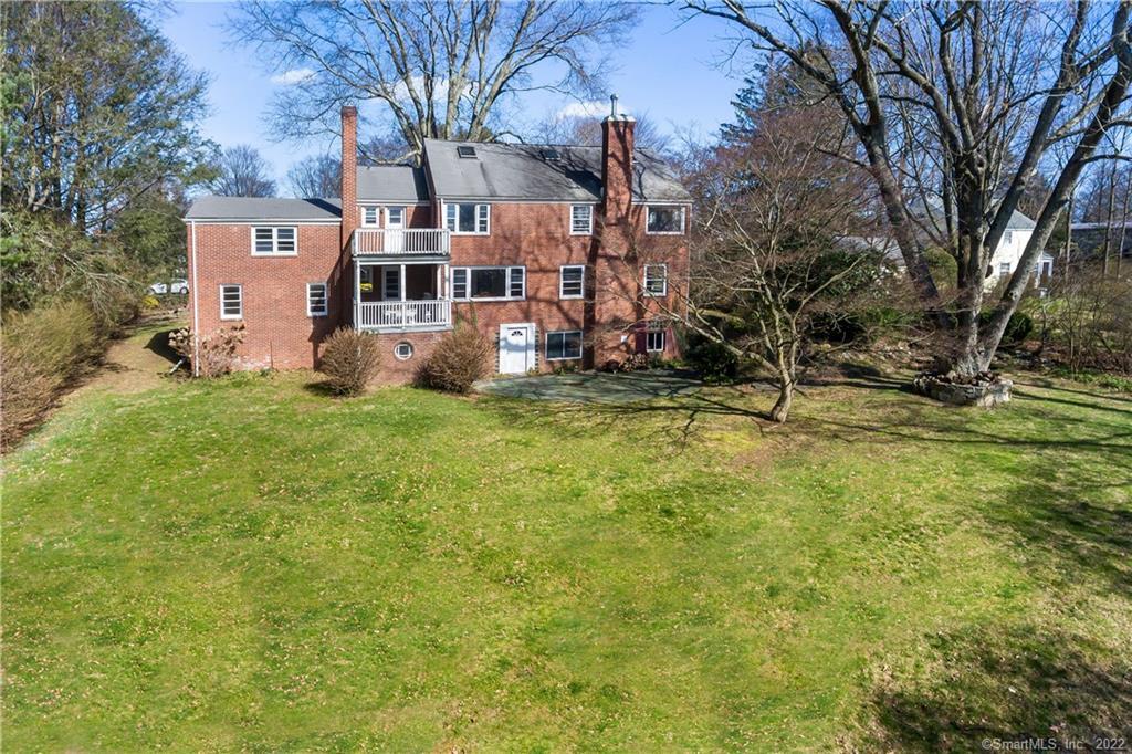 Rear of a brick Fairfield home with two balconies, mature trees, and a broad lawn.