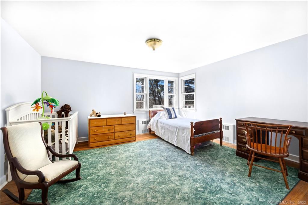 Bedroom with a white crib, single bed beneath bay windows, and green patterned rug.