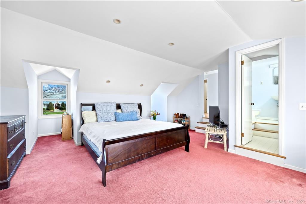 Furnished bedroom with a dark wood bed, pink carpet, sloped ceiling, and adjoining bathroom.