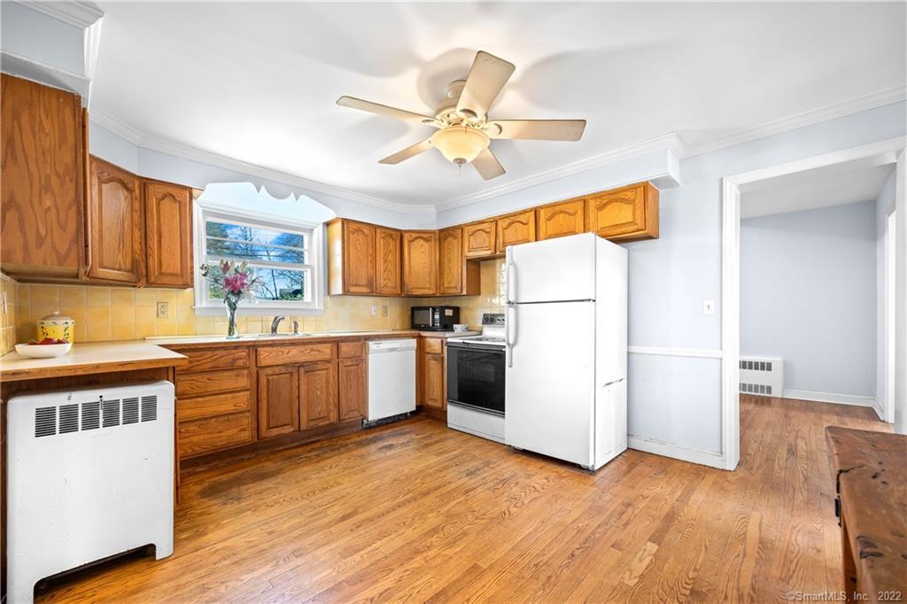 Kitchen with wood cabinets, yellow tile backsplash, hardwood floors, and white appliances.