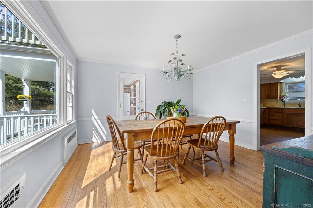Dining room with a wooden table, chandelier, hardwood floors, and large windows overlooking a porch.