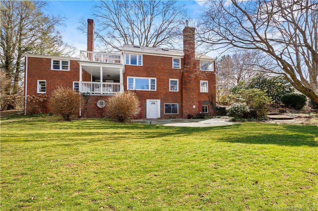 Red-brick home with white-railed balconies and tall chimneys beyond a broad lawn.
