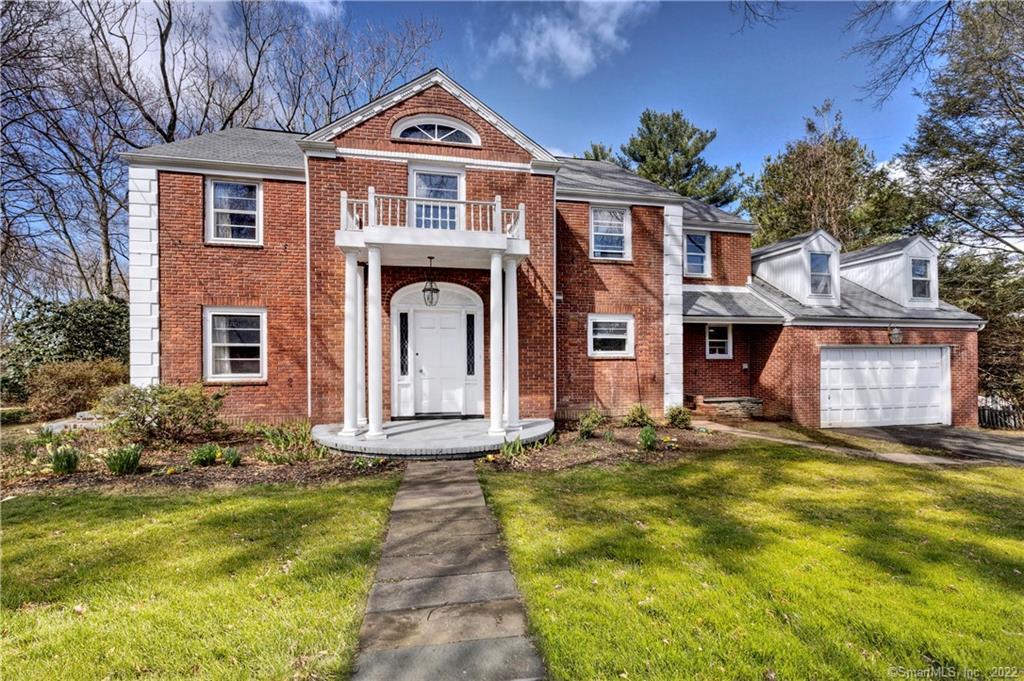 Red brick house with a white columned entrance, balcony, attached garage, and front lawn.