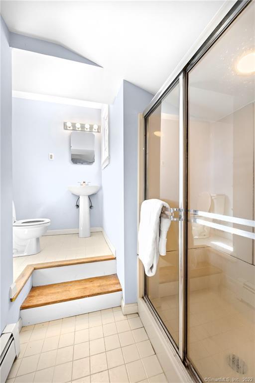 Bathroom with a glass-enclosed shower and toilet and sink on a raised platform.
