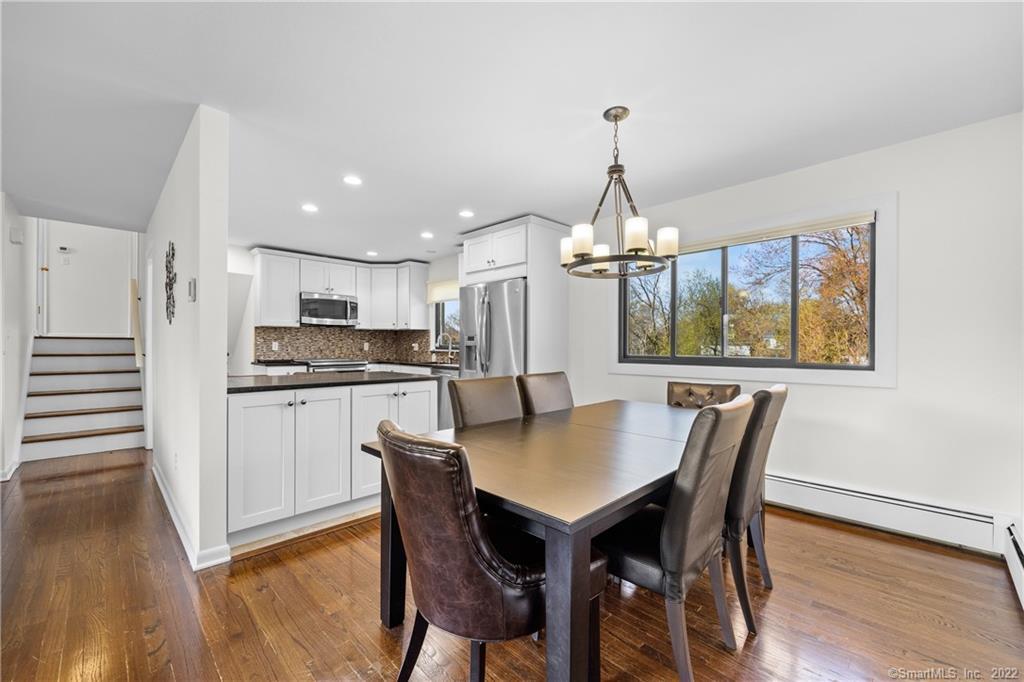 Kitchen and dining area with white cabinets, stainless appliances, hardwood floors, and a large window.