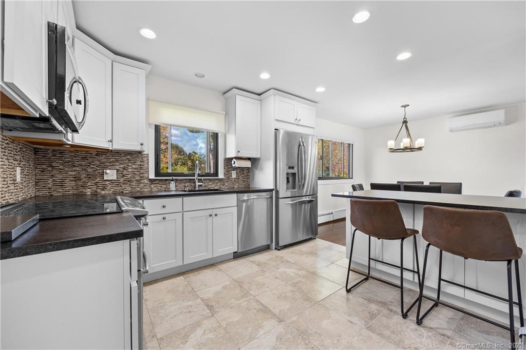 Bright white kitchen with stainless-steel appliances, dark countertops, and an adjoining dining area.