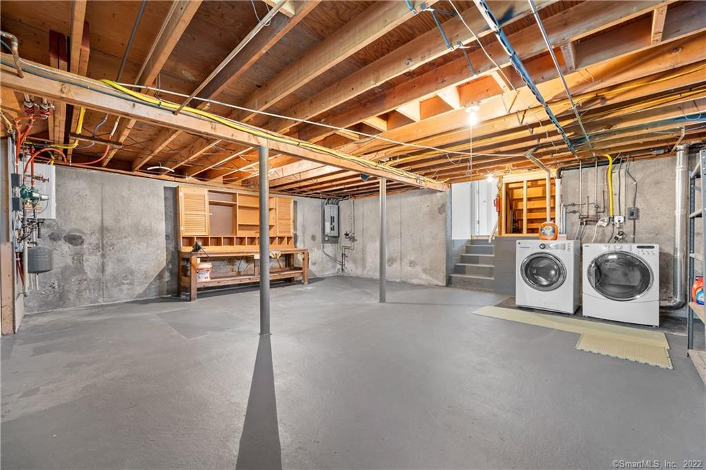 Unfinished basement with exposed ceiling joists, a workbench, and washer and dryer.