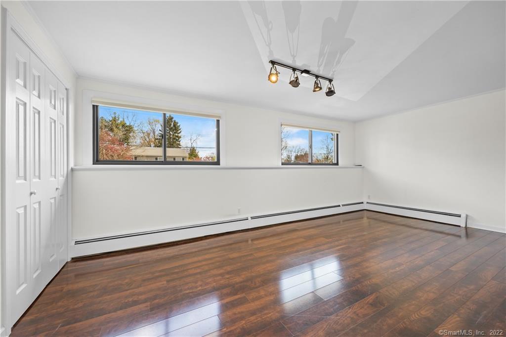 Empty bedroom with hardwood floors, two windows, and a wall of closet doors.