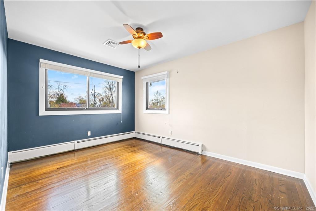 Vacant bedroom with hardwood floors, a ceiling fan, and a dark blue accent wall.