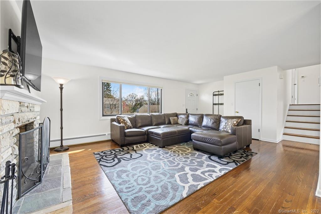 Living room with a gray sectional, patterned rug, hardwood floors, and a stone fireplace.