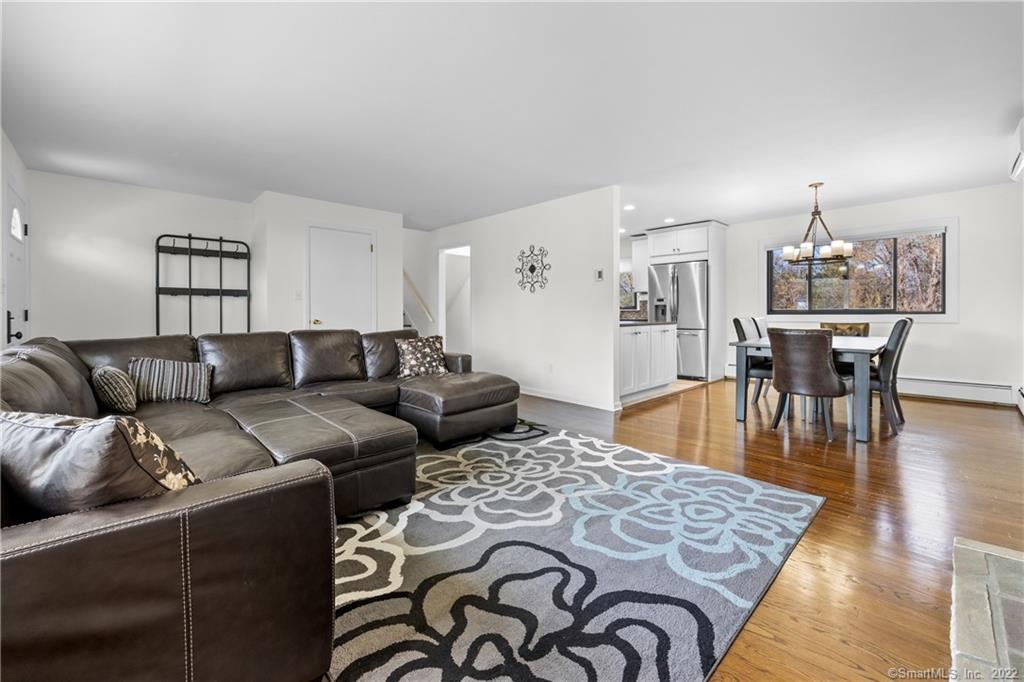 Open-plan living and dining area with a leather sectional, patterned rug, hardwood floors, and white kitchen.