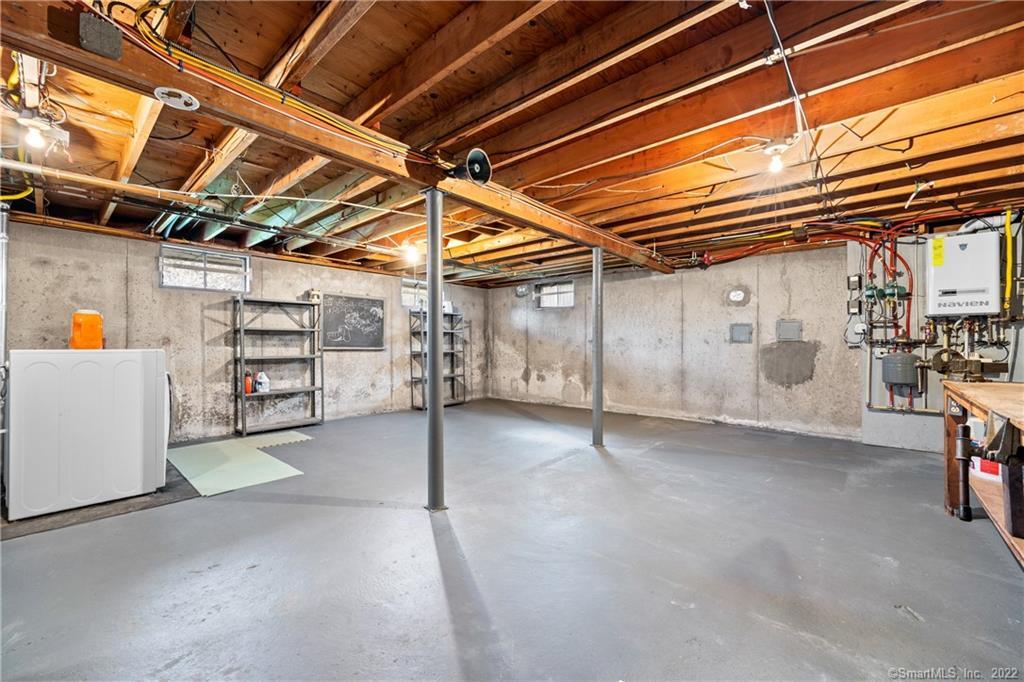 Unfinished basement with exposed wooden ceiling joists, concrete floor, support posts, and utility equipment.