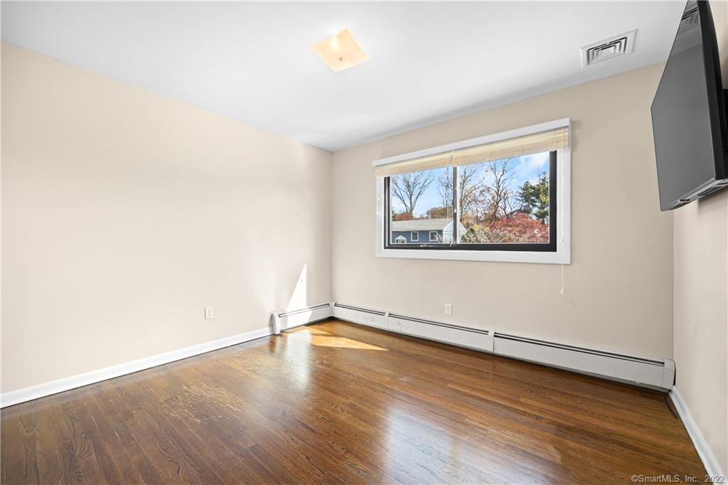 Empty bedroom with polished hardwood floors, a wide window, baseboard heating, and a wall-mounted television.
