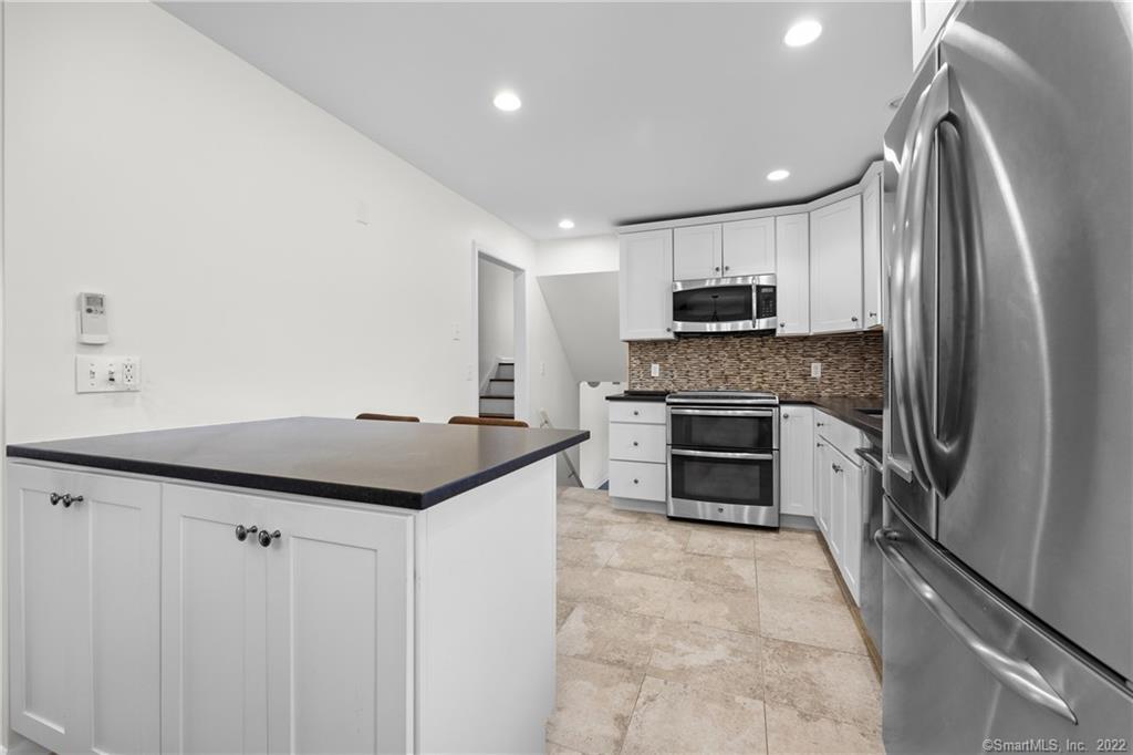 Kitchen with a dark-countertop island, stainless steel appliances, and white cabinets.