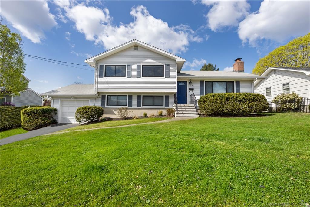 White split-level home with a blue front door, attached garage, and broad green lawn.