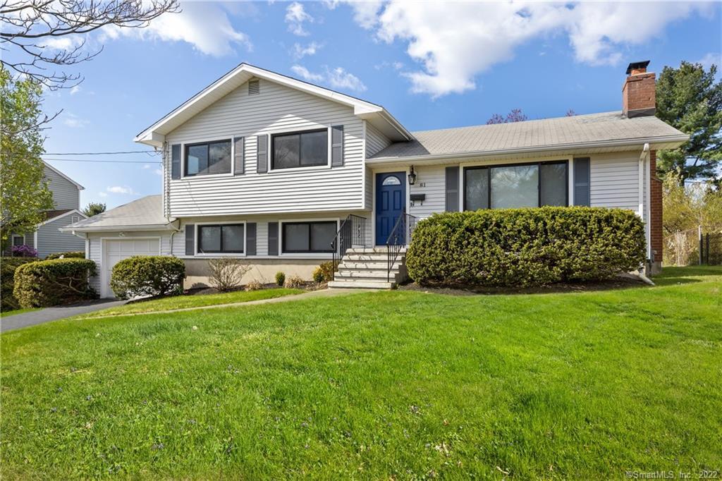 White split-level house with a blue front door, attached garage, and broad green lawn.
