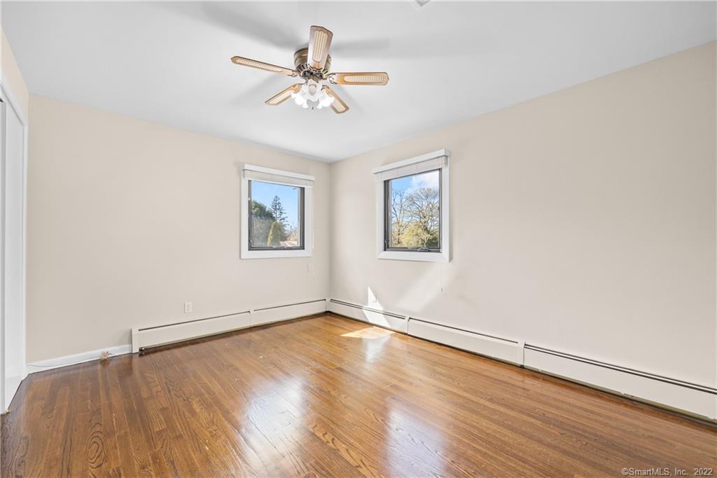 Empty bedroom with polished hardwood floors, two windows, and a ceiling fan.