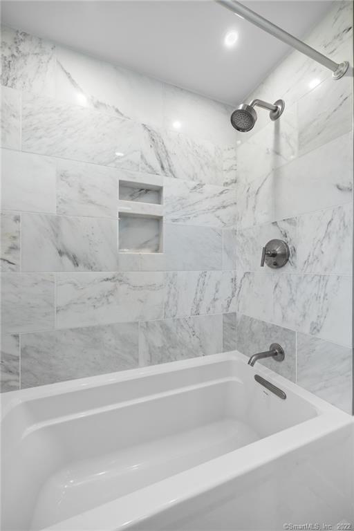 Marble-tiled bathtub and shower with recessed wall niches and chrome fixtures.
