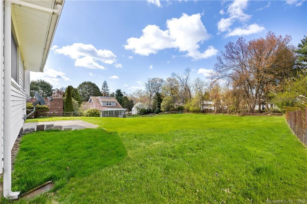 Backyard with a broad green lawn, paved patio, and mature trees.