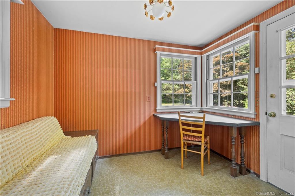 Small room with orange striped wallpaper, a cream sofa, and a desk beneath corner windows.