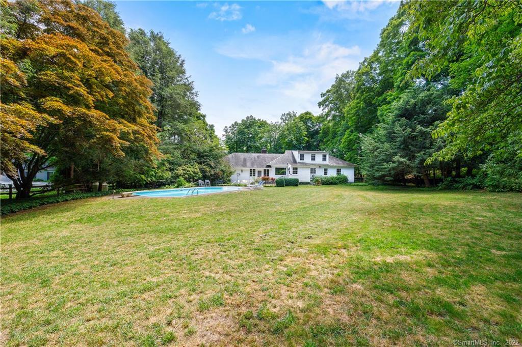 White house beyond a broad lawn, with a swimming pool and mature trees.