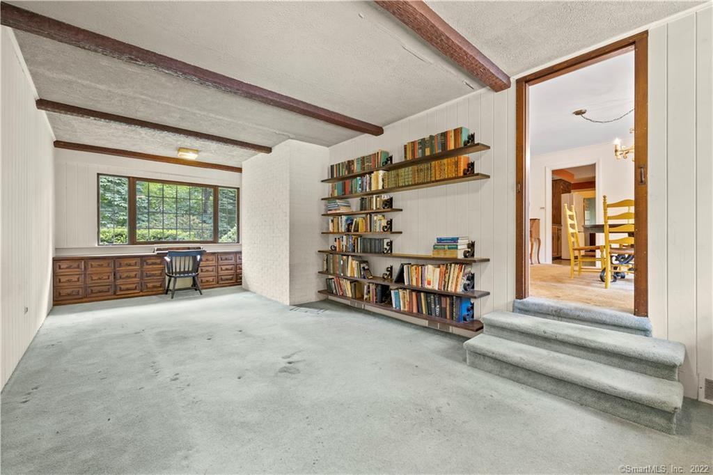 Study with wall-mounted bookshelves, wooden drawers beneath a wide window, and carpeted steps to the adjoining dining room.