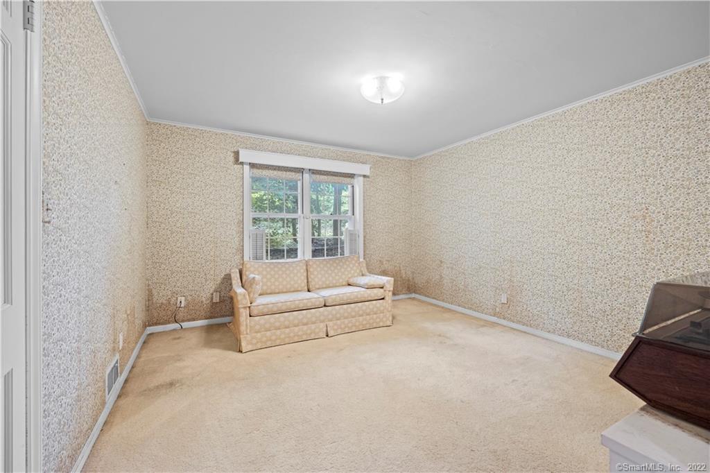 Carpeted living room with patterned wallpaper, a beige sofa, and a large window.