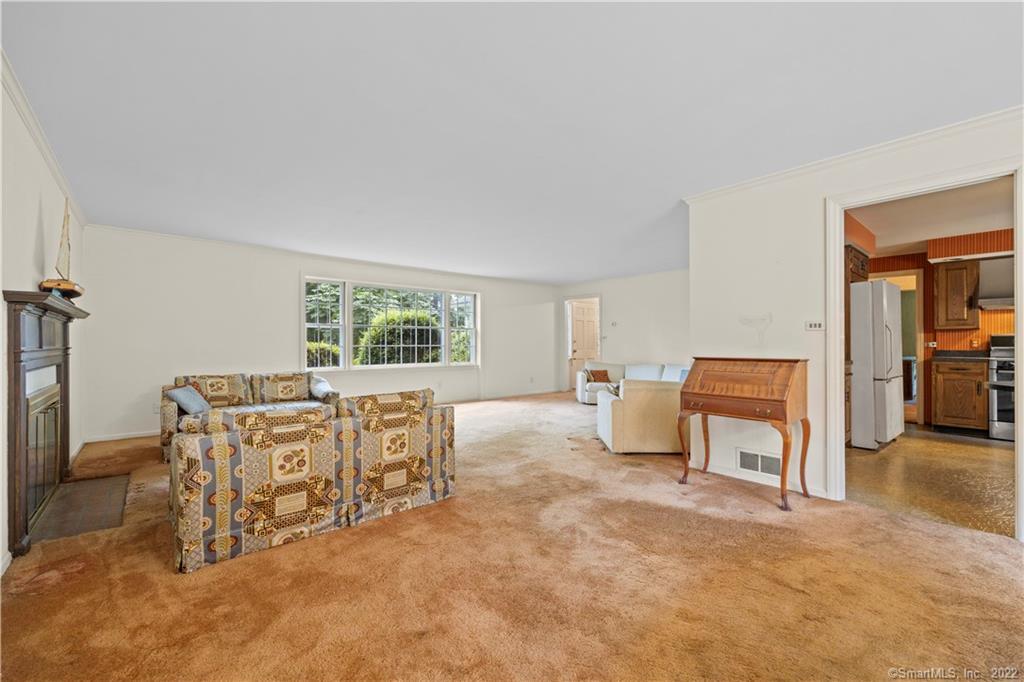 Living room with patterned sofas, beige carpet, a fireplace, and a wide window overlooking trees.
