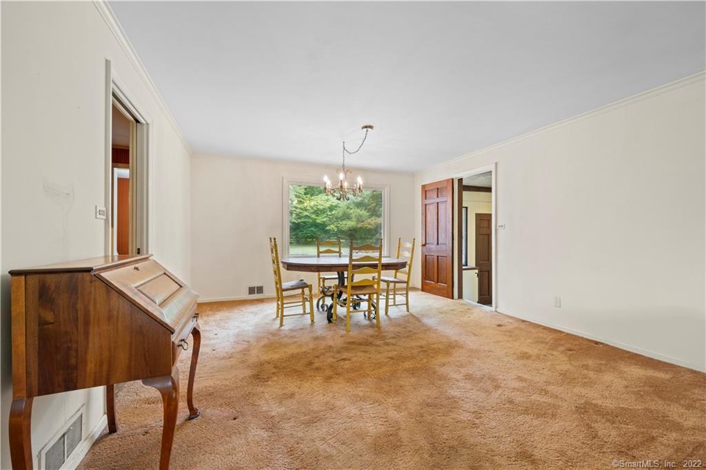 Dining room with tan carpet, a round table beneath a chandelier, and a wooden piano.