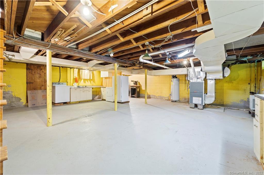 Unfinished basement with exposed ceiling joists, yellow walls, concrete floor, and laundry appliances.