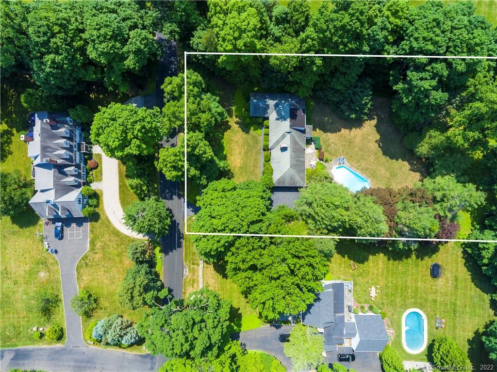 Aerial view of a house and swimming pool on a tree-lined lot outlined in white.