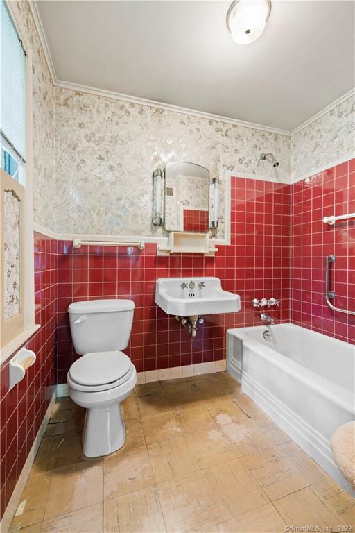 Bathroom with red tile walls, a white bathtub, toilet, and wall-mounted sink.