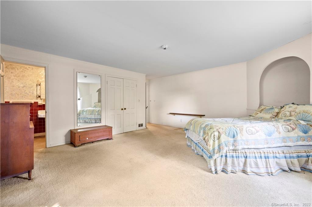 Bedroom with beige carpet, a bed in an arched alcove, and an adjoining bathroom.