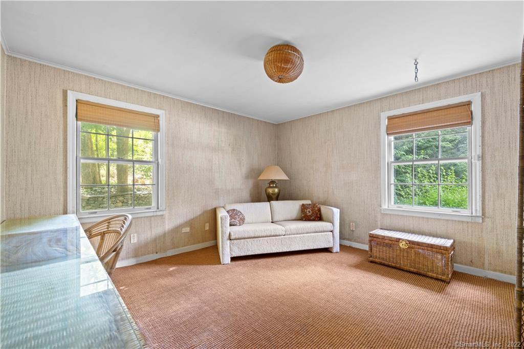 Sitting room with a white sofa, wicker chest, and two windows overlooking greenery.