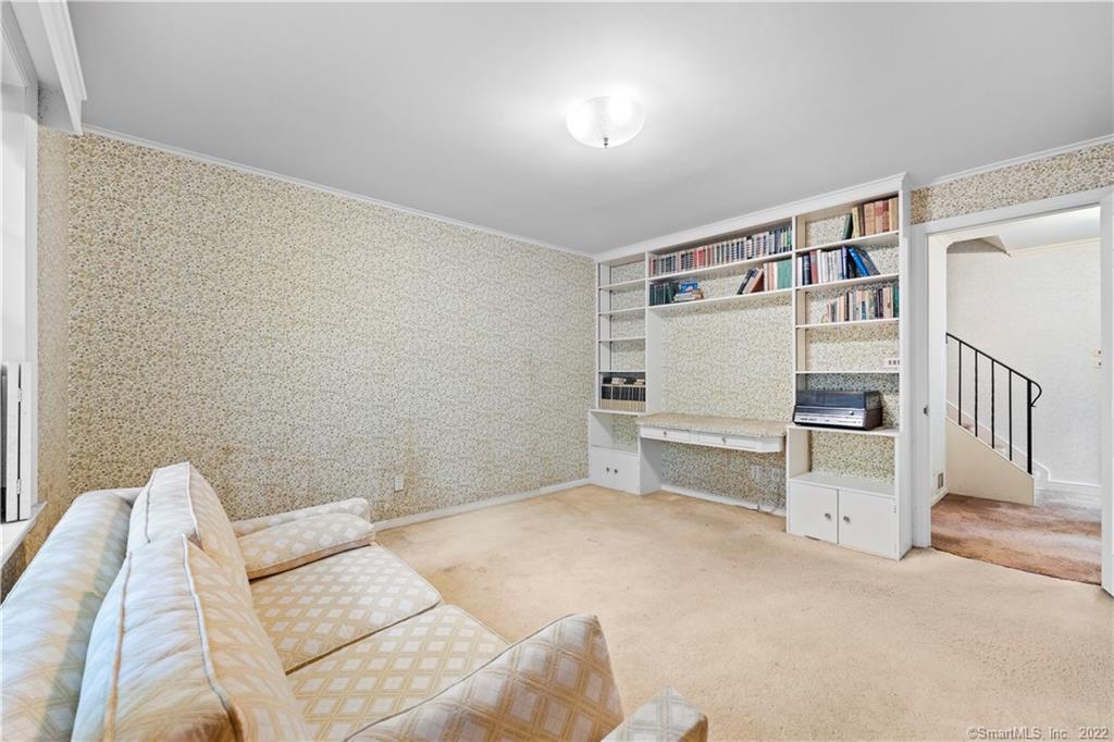 Living room with built-in bookshelves and desk, patterned wallpaper, and a beige sofa.
