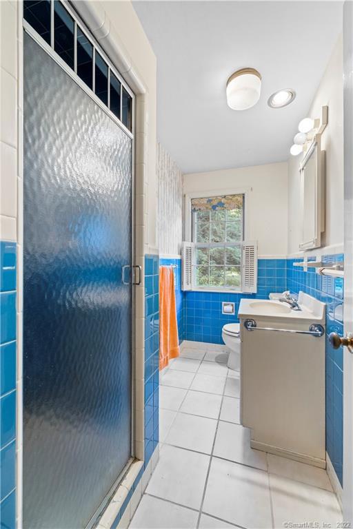Bathroom with blue tile, a frosted-glass shower door, and a window with shutters.