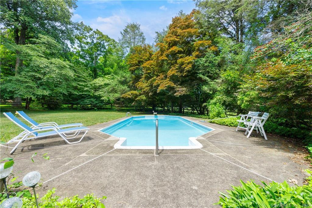 Swimming pool with a concrete patio, lounge chairs, and mature leafy trees.